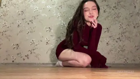 Young woman in a burgundy long-sleeve dress sitting on a floor against floral wallpaper with a dreamy mood.