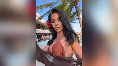 Beautiful woman in a brown bikini with a red flower in her hair posing at a tropical beach resort.