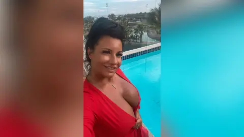 MissyJolie smiles while wearing a red low-cut top next to a bright blue swimming pool.