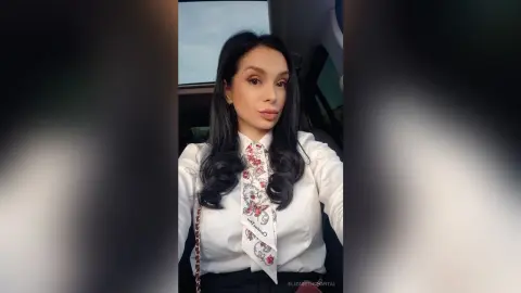 ElizabethChantal — Elegant woman in a white blouse and floral tie posing inside a car with a soft, moody aesthetic.