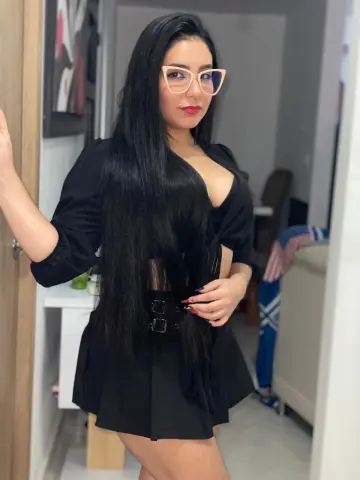 ViolettaBlacke with long black hair and glasses poses in a black outfit, showing cleavage in a mirror selfie.