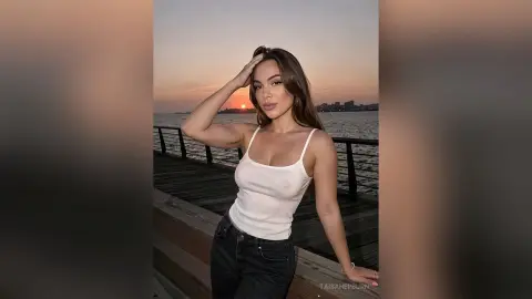 Young woman in a white tank top and jeans posing on a wooden pier during a golden sunset over the ocean.