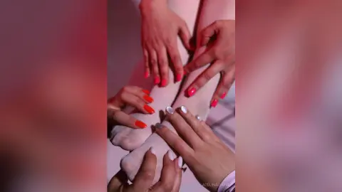 Close-up of manicured hands and feet with bright red and white nail polish in soft, moody pink lighting.