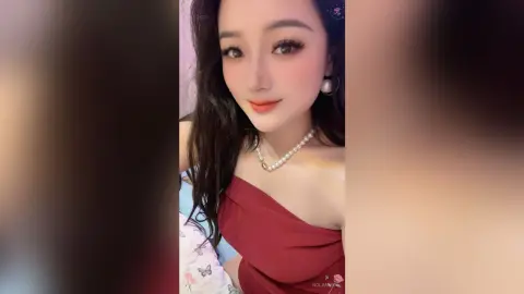 Beautiful young woman in a red strapless dress and pearl necklace posing with a soft, elegant expression.