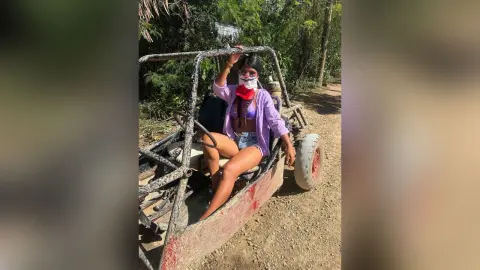 Young woman in a purple shirt and denim shorts sitting on an off-road buggy on a sunny dirt path.