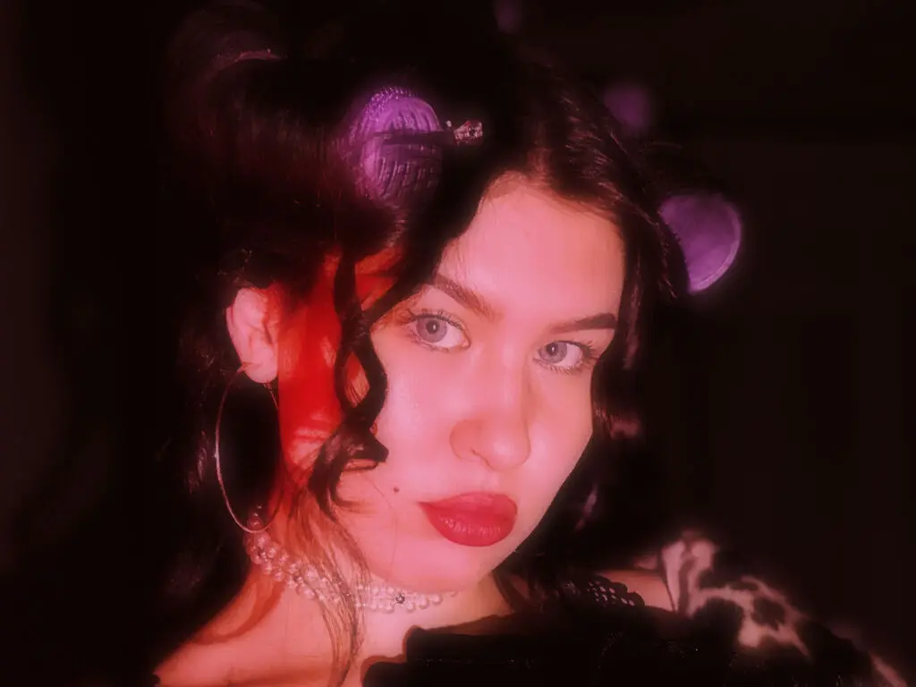 Young woman with curly hair and hoop earrings posing in moody red lighting.