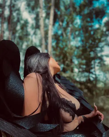 Woman in black lace lingerie relaxing in a dreamy, sun-dappled forest setting.