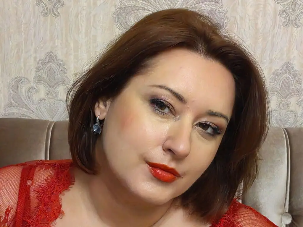 Woman with brown hair and red lipstick wearing a red lace outfit in a cozy indoor setting.