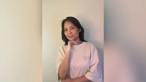 ViolaEbbing poses with a hand on her chin, wearing a loose beige t-shirt against a plain wall.