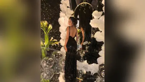 Elegant woman in a black sequin evening gown posing by white floral decor and disco balls at a glamorous party.
