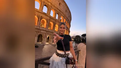 Young woman in a black top and white skirt posing in front of the Roman Colosseum at sunset.