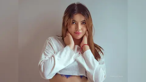 Young woman in a white long-sleeve crop top posing with a serene expression against a neutral background.