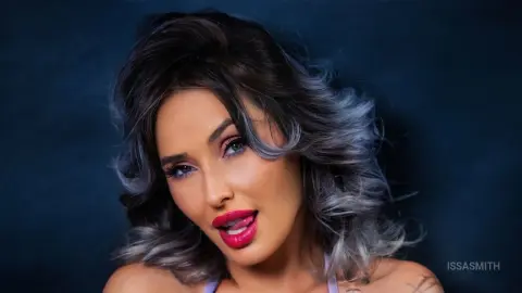 Glamorous woman with wavy silver hair and bold red lipstick posing against a dark moody background.