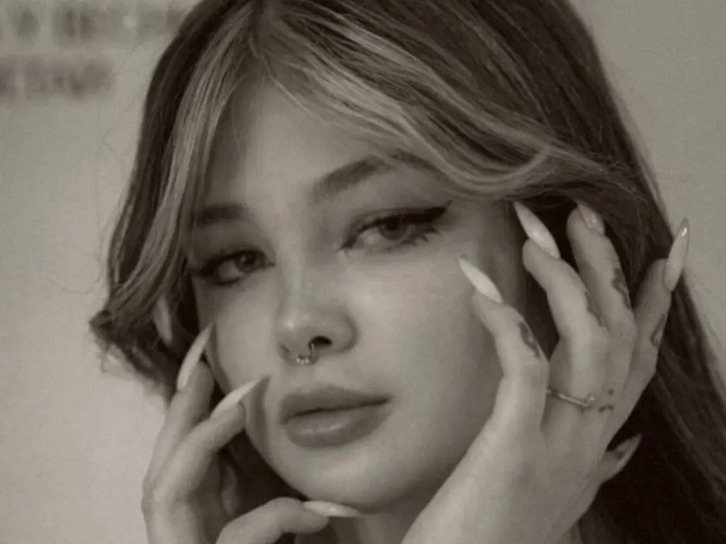 Close-up portrait of a young woman with winged eyeliner and nose ring in a moody black and white aesthetic.