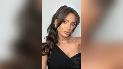 Glamorous woman in a black evening dress and silver jewelry posing with elegant makeup against a white background.