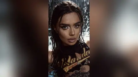 Beautiful woman with wet hair and dramatic makeup wearing a black graphic t-shirt under falling water.