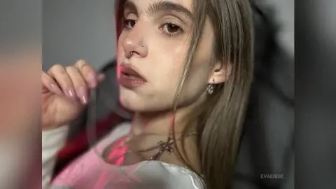Young woman with nose ring and silver jewelry posing in soft, moody lighting.