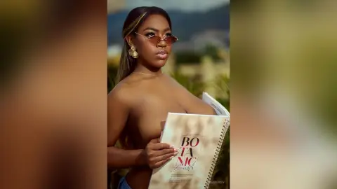 Glamorous woman in sunglasses holding a fashion catalog outdoors in a sunny, chic setting.
