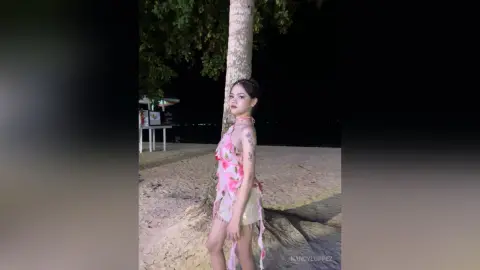 NancyLoppez stands on a sandy beach at night wearing a pink floral halter top and light-colored bottoms.