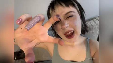 VernellZiccardi poses close to the camera with a hand reaching forward, showing her short dark hair and grey tank top.