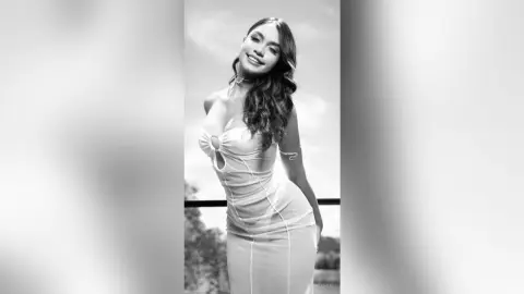 Smiling young woman in a tight white cocktail dress posing outdoors in a black and white portrait.