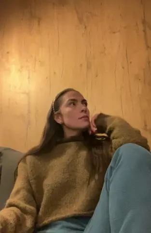 Thoughtful woman in a cozy brown knit sweater relaxing on a sofa against a warm wood wall.