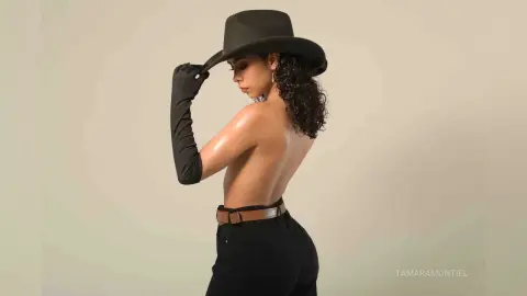 Elegant woman in black hat and long gloves posing with bare back against a neutral studio background.