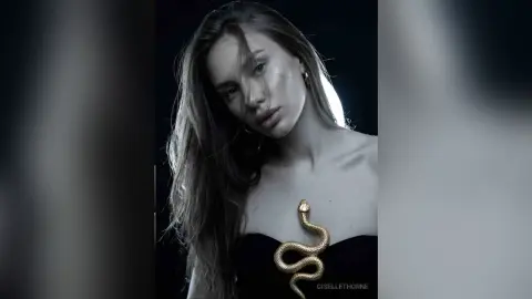 Moody portrait of a woman in a black strapless top with a gold snake accessory against a dark background.