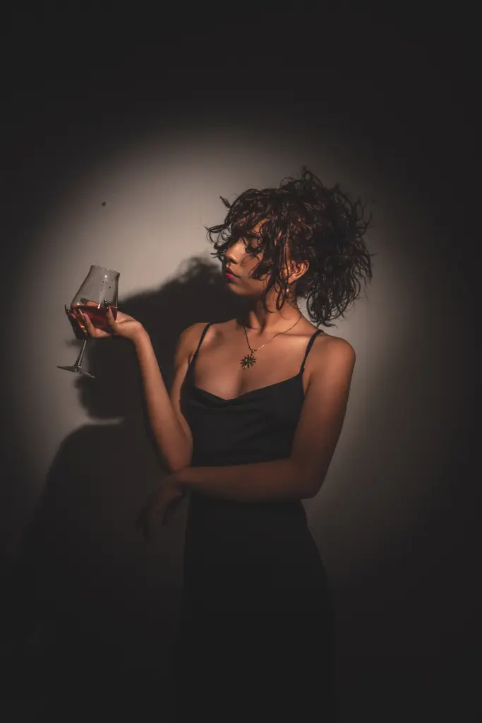 Young woman with curly hair in a black satin camisole posing under dramatic spotlight lighting.