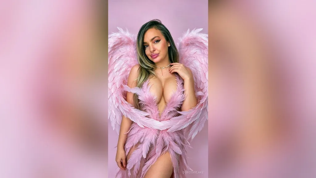 DorothyLake — DorothyLake poses in a pink feathered angel outfit with large matching wings against a pink background.
