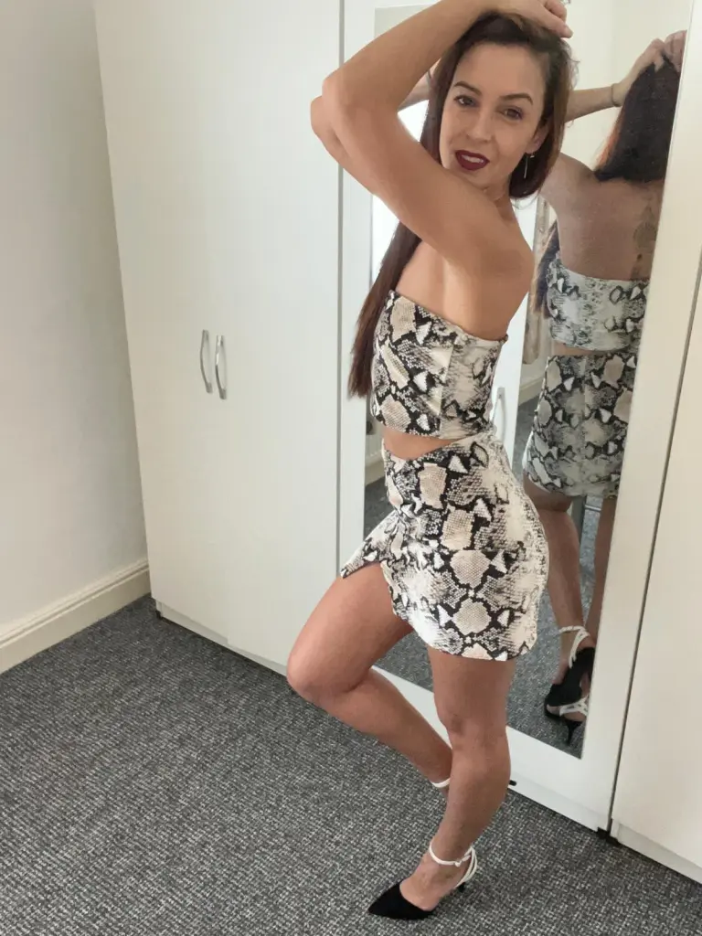 Karlaolivia poses in a silver tube top, showing her long red hair and bare shoulders against a dark background.