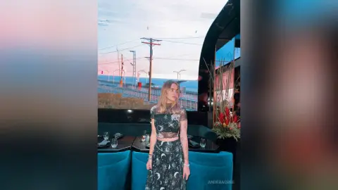 Young woman in a black celestial print crop top and skirt sitting by a window at sunset.