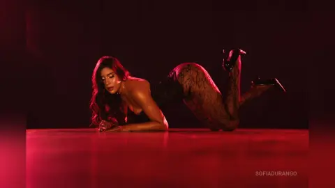 Glamorous woman in black lace bodysuit posing on a red floor under moody, dramatic red lighting.