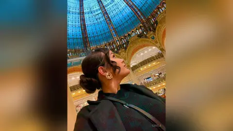 Elegant woman in a black outfit looking up at a grand blue glass dome in a luxury historic building.