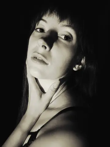 Moody black and white portrait of a young woman with bangs wearing a lace camisole in dramatic lighting.