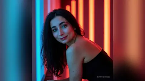 Young woman in a black top posing against a moody background of glowing blue and orange neon lights.