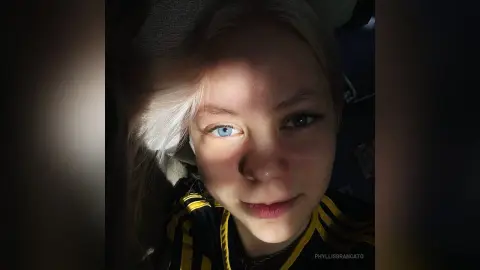 Close-up portrait of a blonde woman in a black and yellow striped shirt with soft, moody lighting.