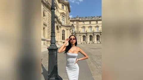 Stylish woman in a white bodycon dress and sunglasses posing against classic Parisian architecture.
