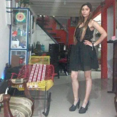 SilvannaReed stands in a room wearing a black mesh dress, posing with one hand on her hip and her long hair down.