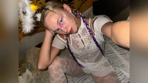 Young woman with purple braids in a white lace outfit posing in a cozy indoor setting.