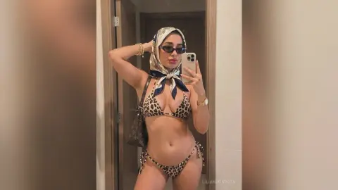 LilianMendoza poses in a mirror wearing a leopard print bikini and a white patterned headscarf with dark sunglasses.