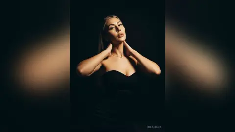Elegant woman in a black strapless dress posing against a dark background with moody studio lighting.