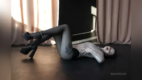 Woman in silver sequin bodysuit and black tights lying on a studio floor in a moody, cinematic setting.