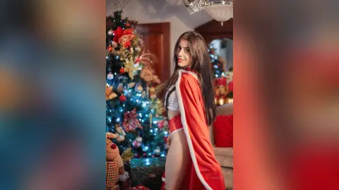 JessieLiu poses in a white and red holiday outfit with long brown hair, standing next to a decorated Christmas tree.