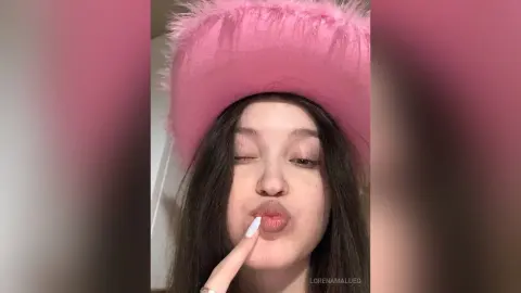 Playful young woman in a pink fuzzy hat making a kissing face in a cozy indoor setting.