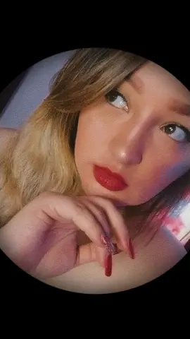 Katiee_and_sharon looks into the camera with red lipstick and long red nails while resting her chin on her hand.