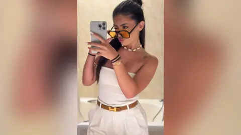 Stylish woman in white strapless top and sunglasses taking a mirror selfie in a bright modern room.