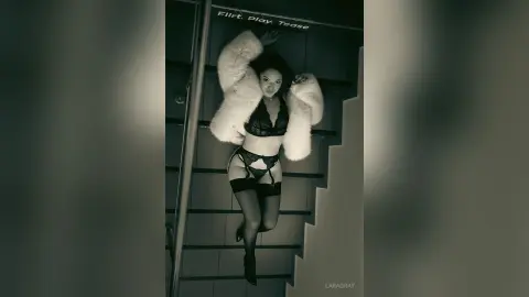 Sultry woman in black lace lingerie and white faux fur coat posing on a staircase in a moody black and white photo.