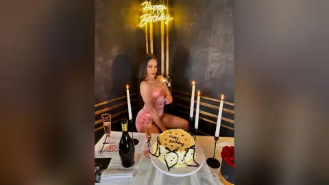 GracieCarter sits behind a birthday cake and lit candles, wearing a pink satin slip dress.