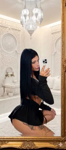 Woman in black outfit taking a mirror selfie in an elegant white Moroccan style room with ornate decor.